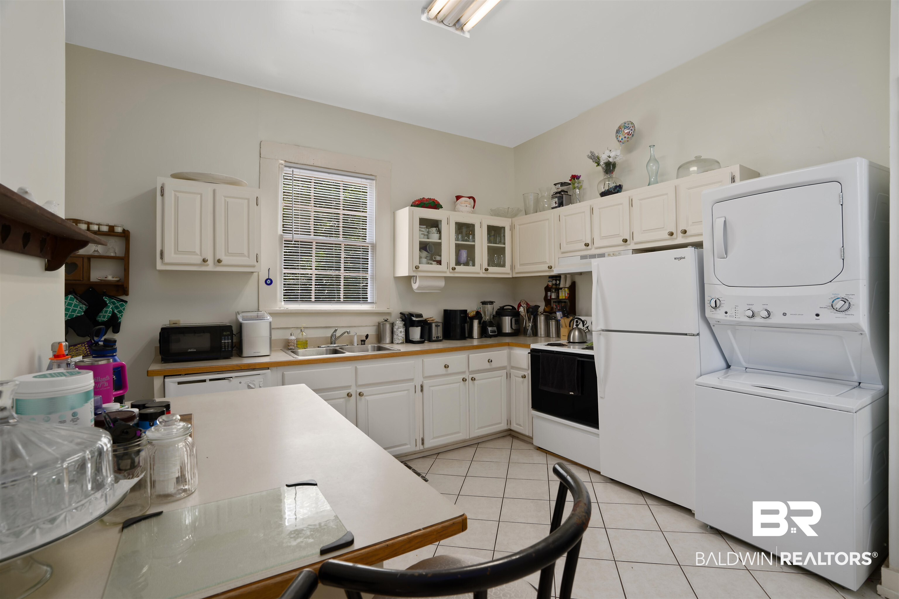 1010 Dauphin Street Mobile, AL 36604 - Photo 13 of 22 Kitchen with white cabinetry, stacked washer / drying machine, light tile patterned flooring, sink, and white appliances