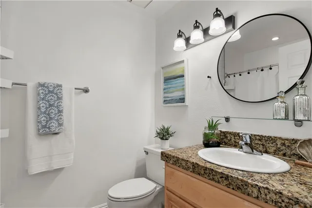 a bathroom with a granite countertop toilet a sink and mirror