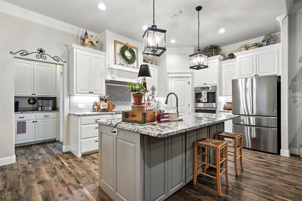 136 Dove Run Tuscola, TX 79562 - Photo 13 of 37 Kitchen featuring stainless steel appliances, decorative backsplash, crown molding, white cabinetry, dark wood-type flooring, and a kitchen island with sink