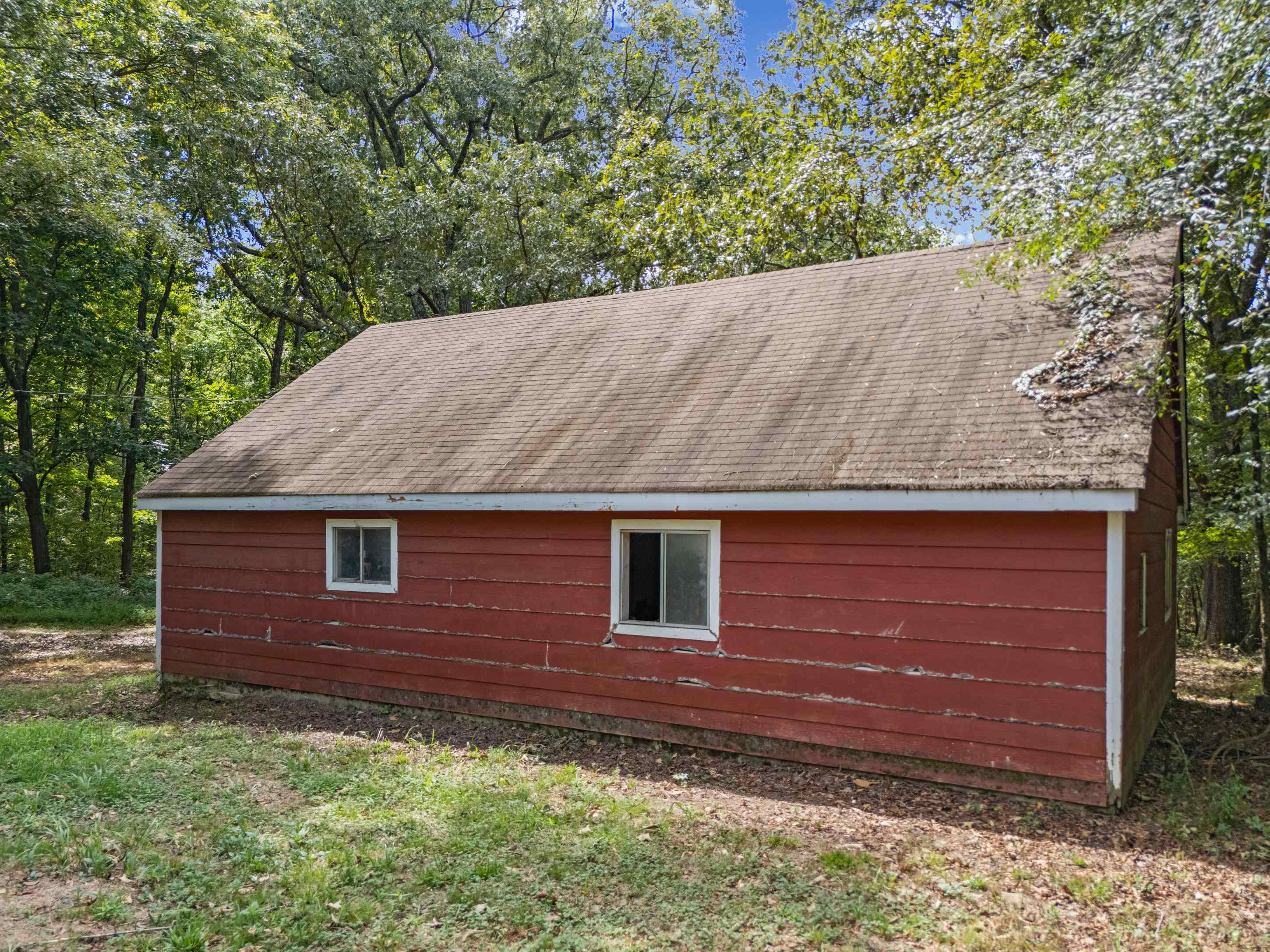 779 Strickland Road Coldwater, MS 38618 - Photo 36 of 40 Red wood-sided outbuilding with two windows, a brown shingle roof, and surrounding greenery