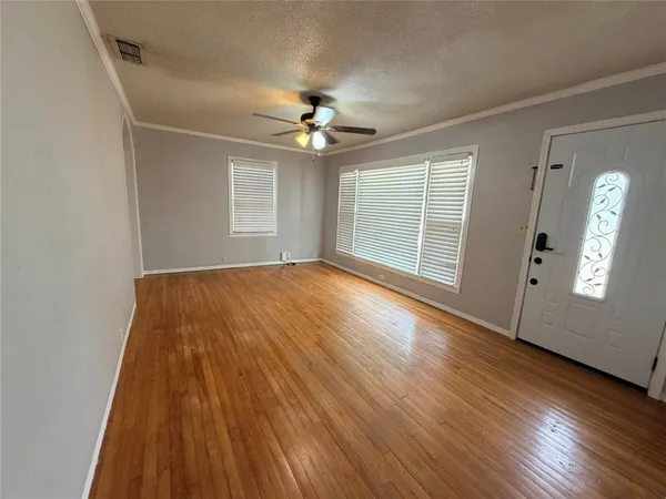 an empty room with wooden floor chandelier fan and windows