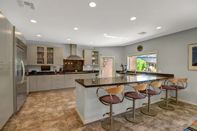 a kitchen with stainless steel appliances granite countertop a stove a sink a refrigerator and chairs