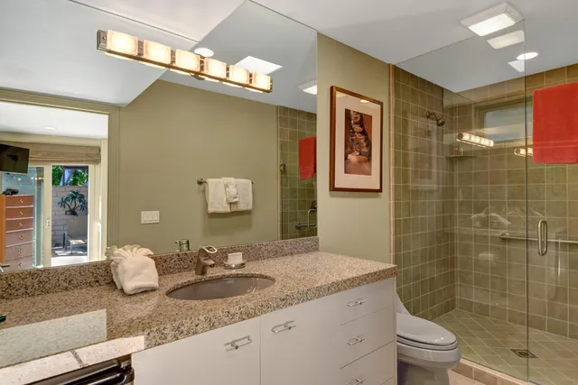 a bathroom with a granite countertop sink a toilet a mirror and shower