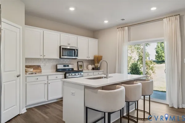 a kitchen with stainless steel appliances granite countertop a stove a sink a microwave a refrigerator with white cabinets and wooden floor