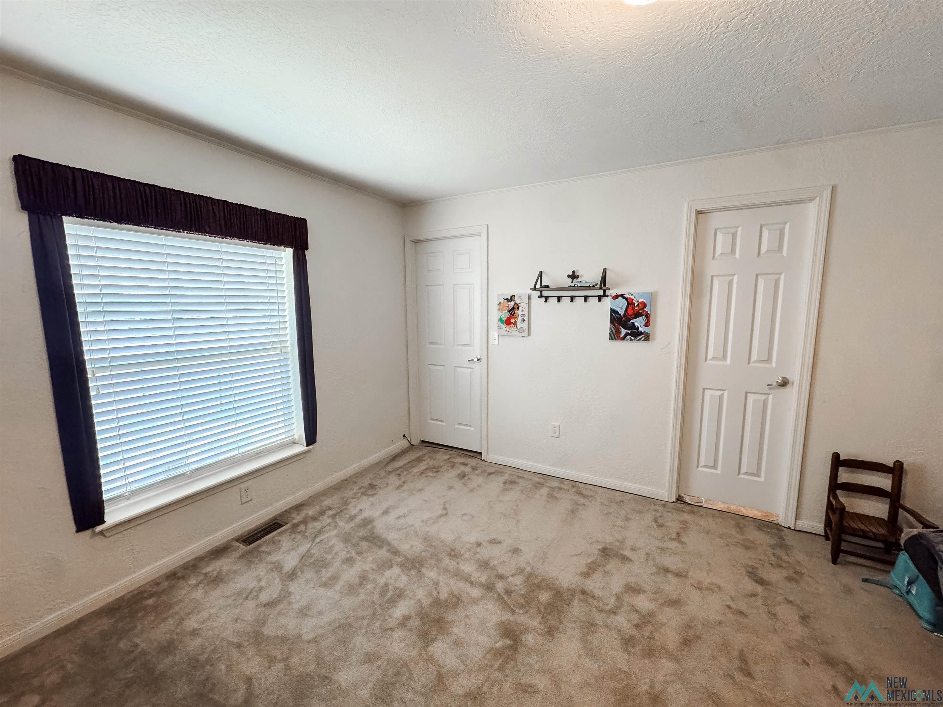 309 Crossbow Road Artesia, NM 88210 - Photo 25 of 31 Carpeted room featuring a large window with blinds, baseboard trim, and two paneled interior doors