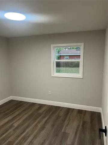 a view of an empty room with wooden floor and a window