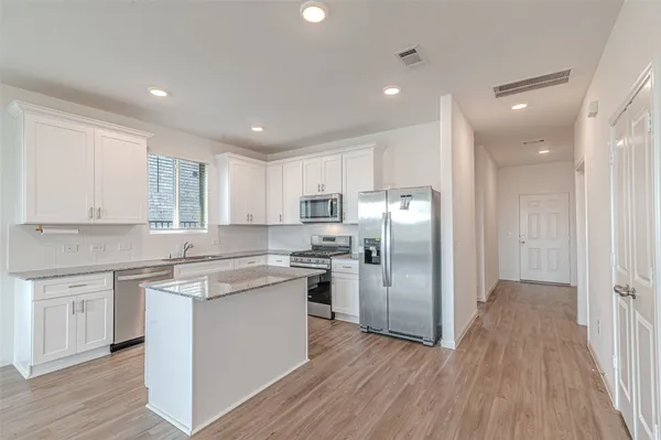 a kitchen with stainless steel appliances granite countertop a refrigerator a sink dishwasher a stove and white cabinets with wooden floor