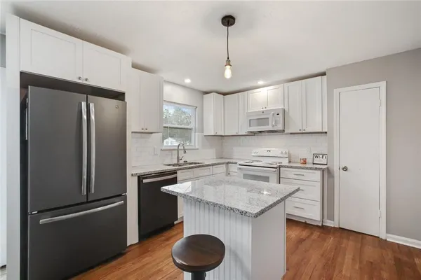 a kitchen with stainless steel appliances granite countertop a refrigerator a sink dishwasher a stove and a microwave oven on the wooden floor