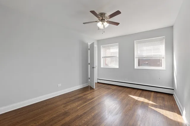an empty room with wooden floor chandelier fan and windows