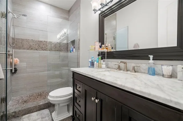 a bathroom with a granite countertop sink a toilet a mirror and shower