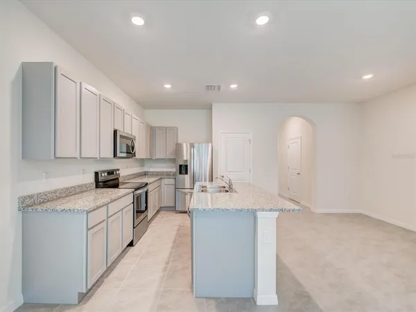 a large white kitchen with stainless steel appliances granite countertop a stove a sink a refrigerator and white cabinets with wooden floor