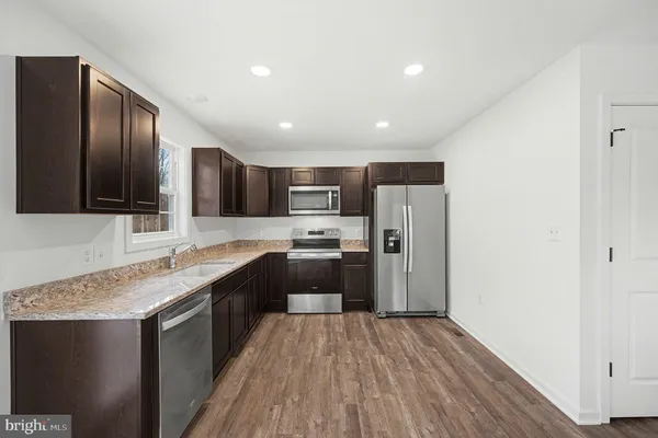 a kitchen with stainless steel appliances granite countertop a refrigerator a sink dishwasher a stove and white countertops with wooden floor