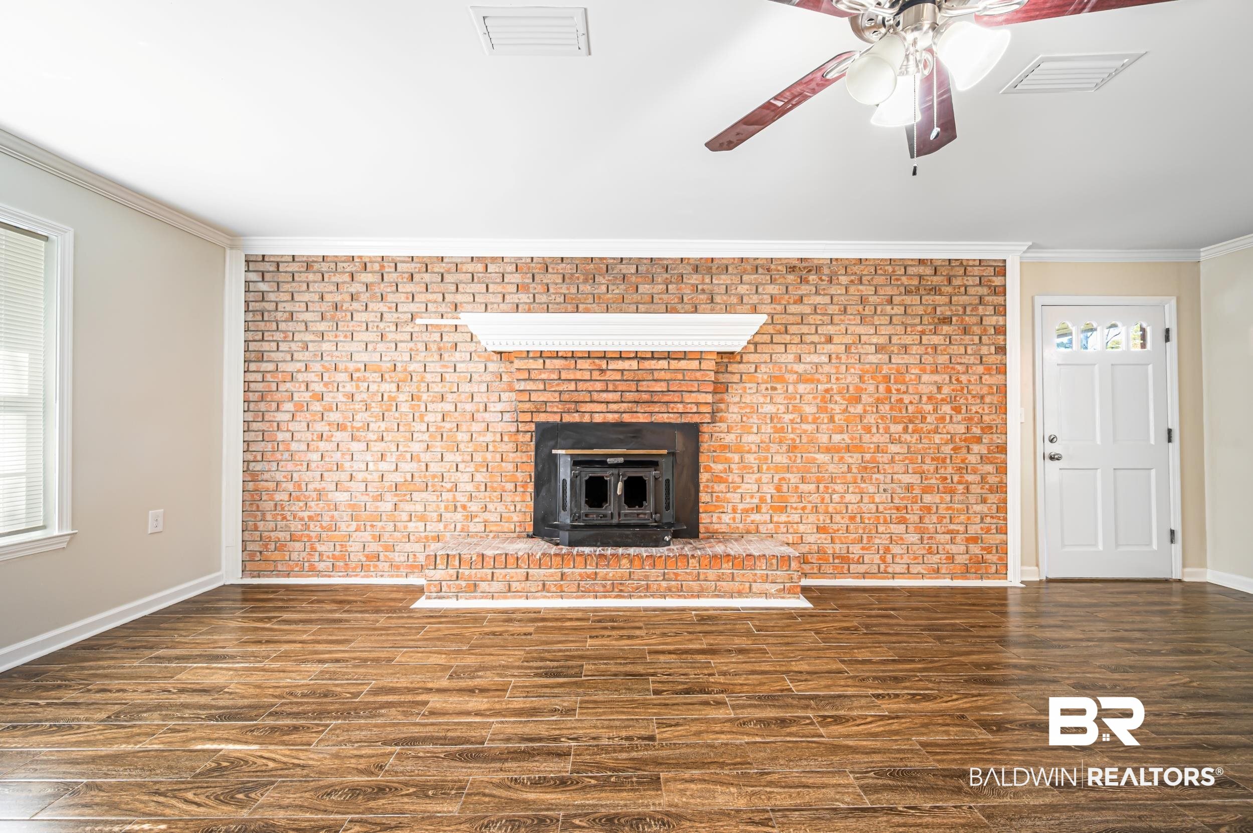 1605 Collier Avenue Bay Minette, AL 36507 - Photo 14 of 36 Unfurnished living room with a wood stove, ornamental molding, dark wood finished floors, brick wall, and ceiling fan