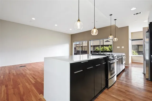 a kitchen with stainless steel appliances granite countertop a sink a stove top oven a counter space and wooden floor