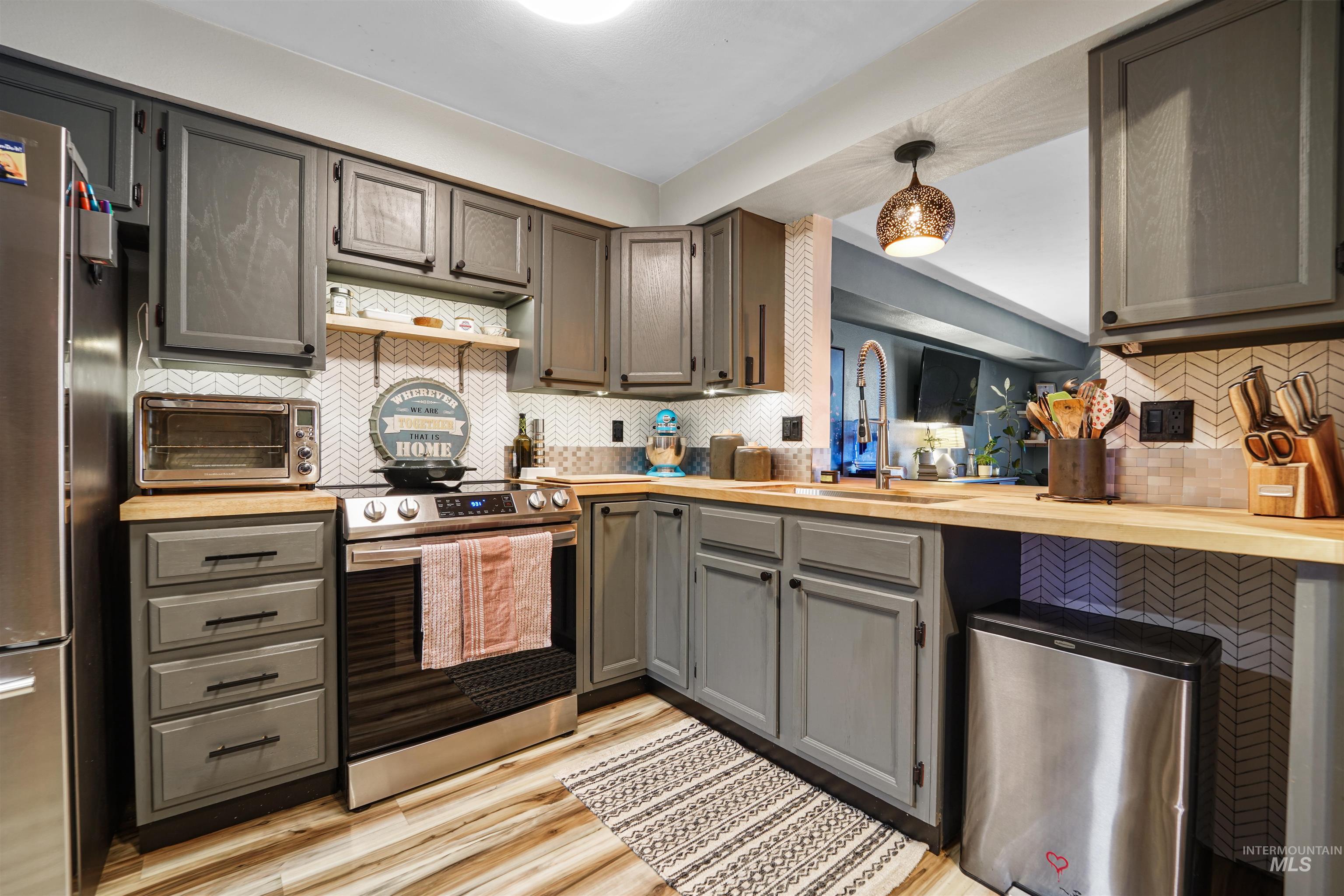 348 North Eagle Road Eagle, ID 83616 - Photo 6 of 31 Kitchen with appliances with stainless steel finishes, backsplash, light wood-style floors, gray cabinetry, and pendant lighting