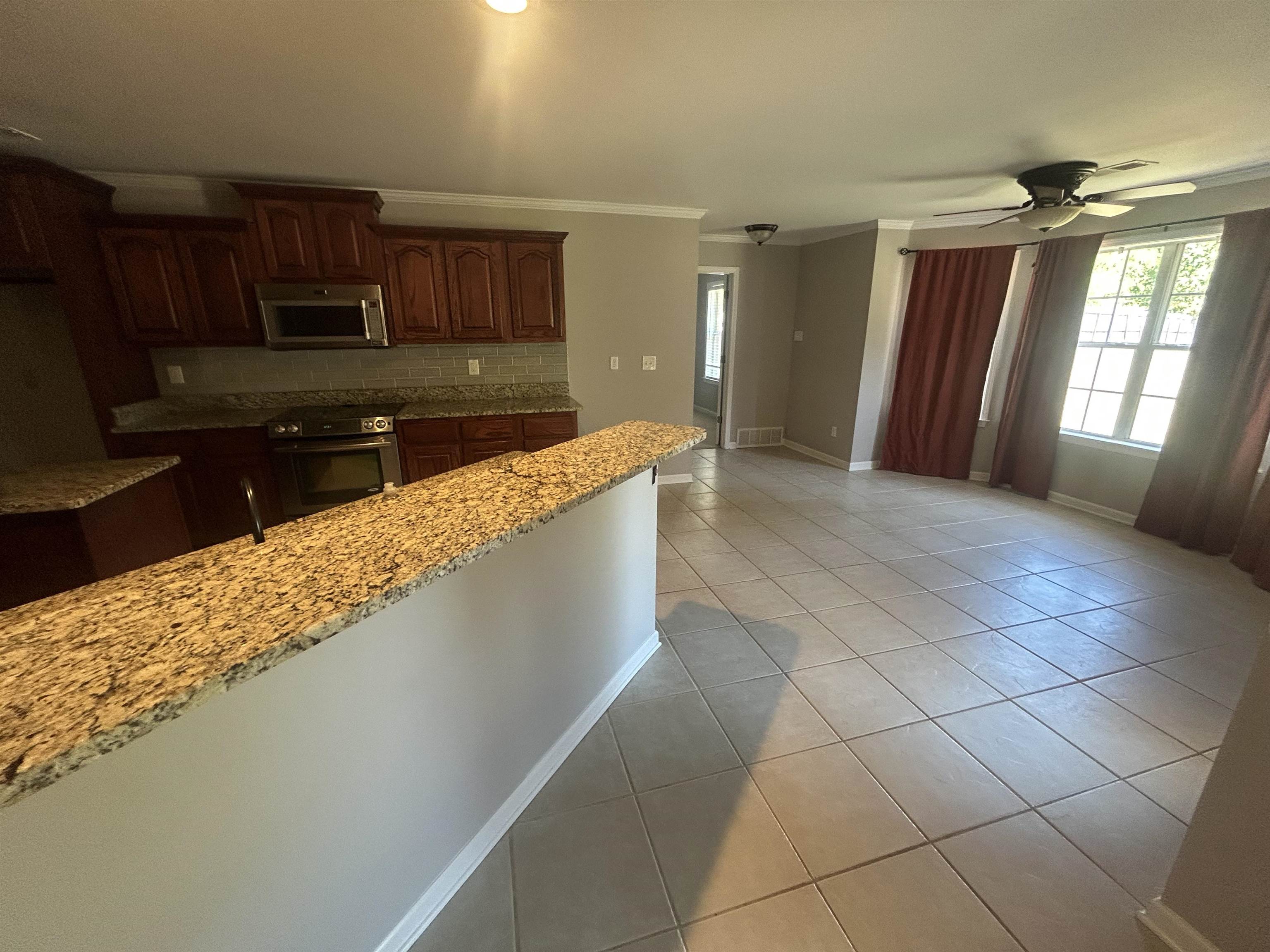 9958 Idaville Road Atoka, TN 38004 - Photo 3 of 20 Kitchen with light tile patterned flooring, light stone counters, crown molding, stainless steel microwave, and ceiling fan