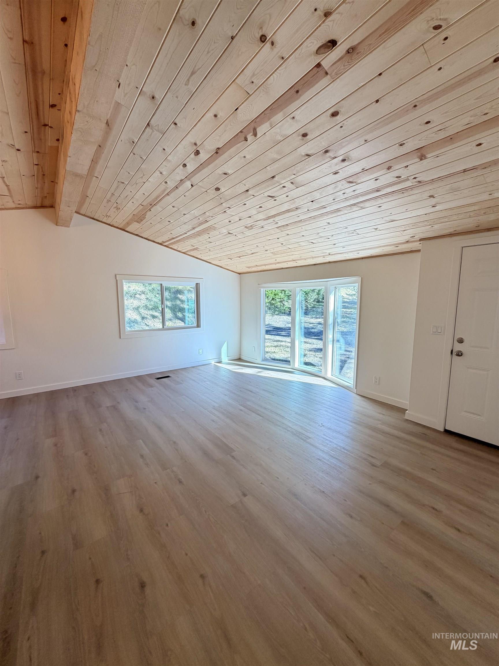 151 View Road Kamiah, ID 83536 - Photo 14 of 49 Vaulted wood-plank ceiling with exposed beam, wood-finish flooring, white walls, multiple windows, and a glass-paneled door