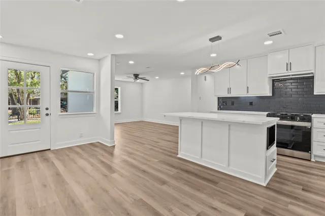 a large kitchen with stainless steel appliances granite countertop a stove a sink white cabinets and a wooden floor