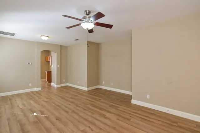 an empty room with wooden floor chandelier fan and windows