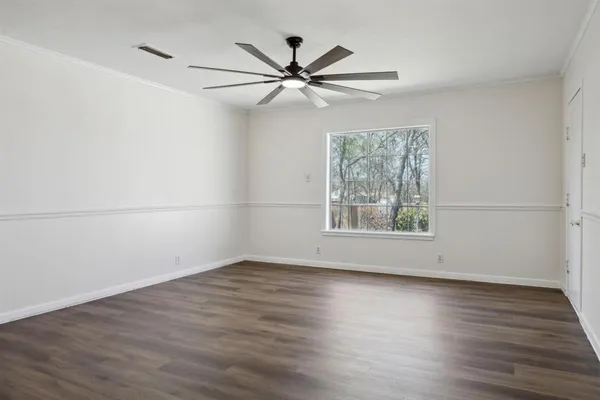 an empty room with wooden floor fan and windows