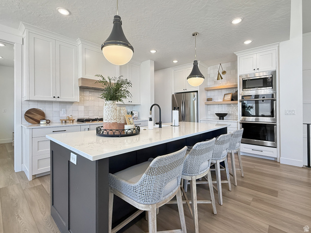 916 Rocky Mountain Way Elk Ridge, UT 84651 - Photo 14 of 54 Dual tone kitchen with two tone cabinetry, tasteful backsplash, stainless steel appliances, a kitchen island with sink, and hanging light fixtures