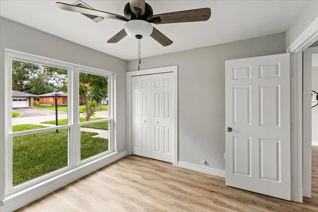 an empty room with wooden floor fan and windows