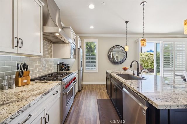 a kitchen with stainless steel appliances granite countertop a sink stove a refrigerator a dining table and chairs with wooden floor