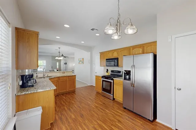 a kitchen with stainless steel appliances granite countertop a refrigerator a sink dishwasher a oven and a dining table with wooden floor