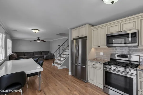 a kitchen with stainless steel appliances a stove a sink dishwasher a refrigerator white cabinets and wooden floor