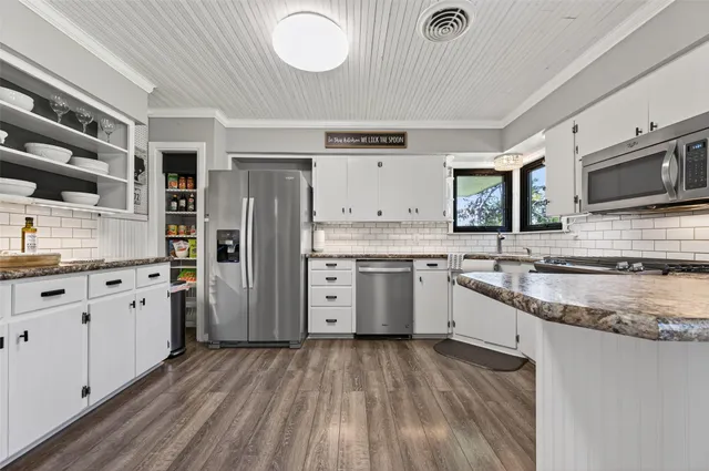 a kitchen with stainless steel appliances granite countertop a stove top oven a sink dishwasher and a refrigerator with wooden floor