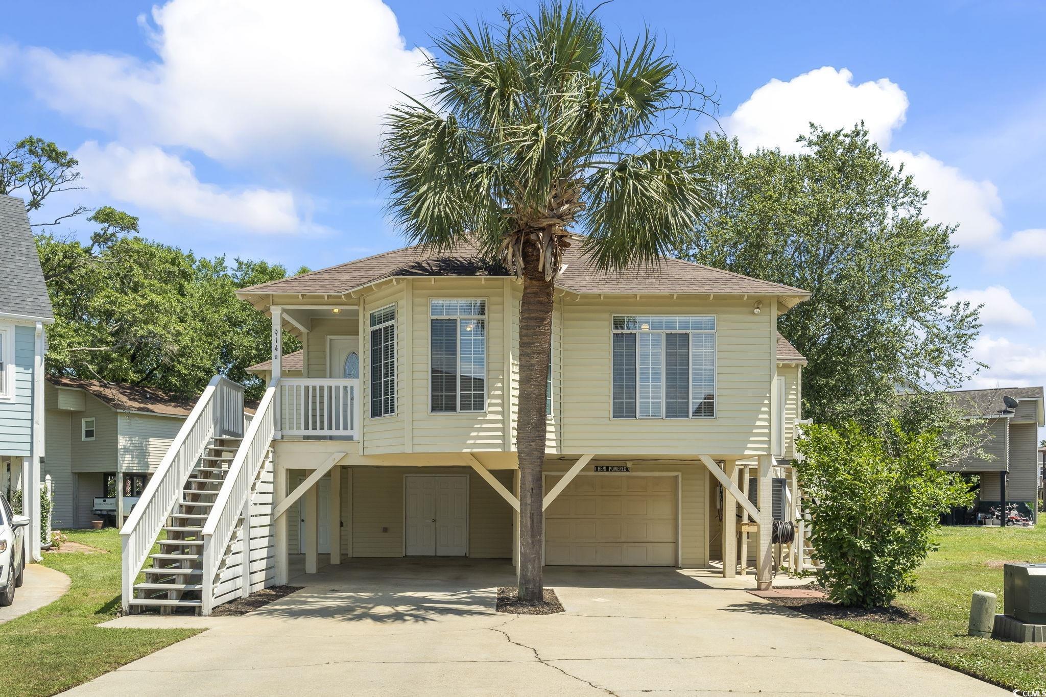 Beach home with stairs, driveway, a garage, and roof with shingles