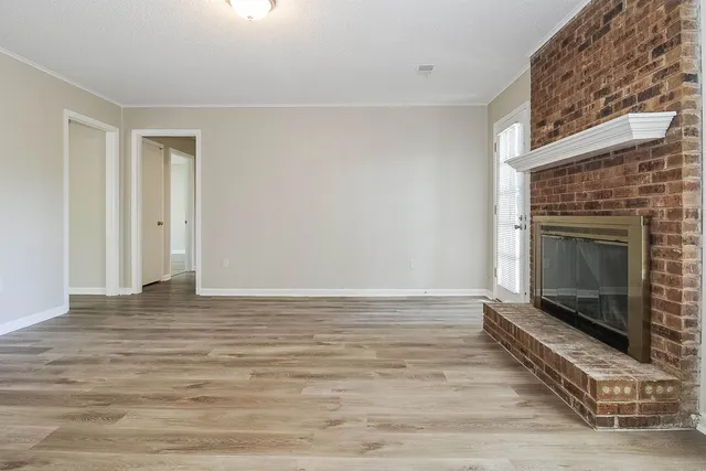 a view of an empty room with wooden floor fireplace and a window