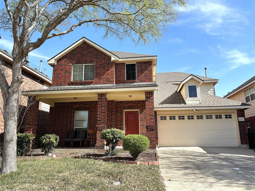 Traditional-style home featuring roof with shingles, driveway, covered porch, brick siding, and a garage