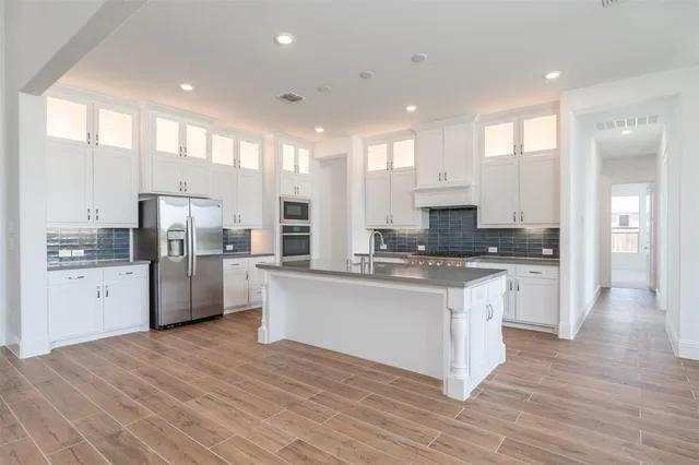 a large kitchen with stainless steel appliances lot of white cabinets and wooden floor