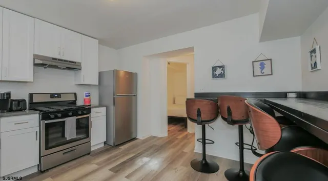 a kitchen with stainless steel appliances granite countertop a stove top oven a refrigerator a dining table and chairs with wooden floors