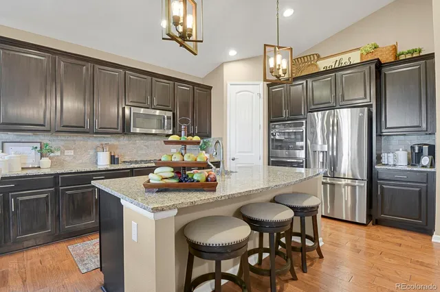 a kitchen with stainless steel appliances granite countertop a sink a stove a refrigerator cabinets a dining table and chairs