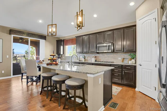 a kitchen with stainless steel appliances granite countertop a stove top oven a refrigerator a sink and chairs