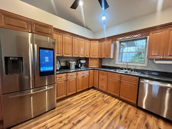 a kitchen with stainless steel appliances granite countertop a refrigerator a sink dishwasher a stove and white countertops with wooden floor