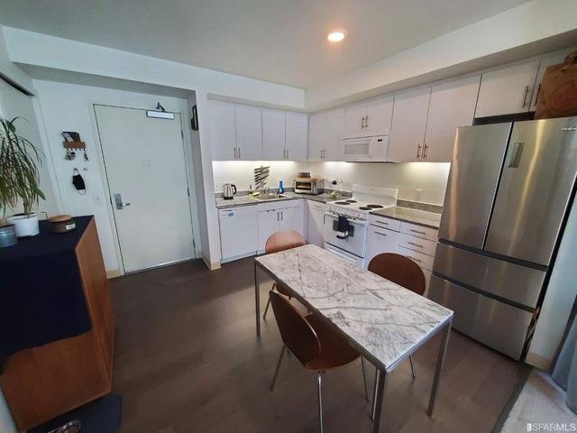 a kitchen with stainless steel appliances granite countertop a refrigerator a stove a sink dishwasher and white cabinets with wooden floor