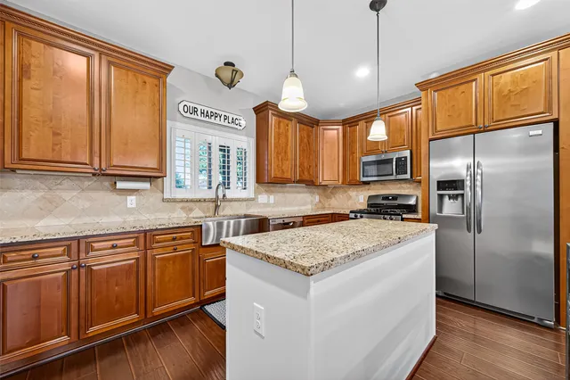 a kitchen with stainless steel appliances granite countertop a refrigerator a sink dishwasher a stove and white countertops with wooden floor