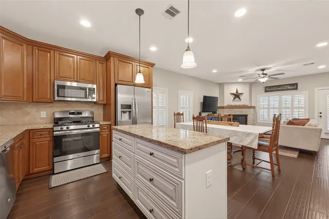 a kitchen with stainless steel appliances granite countertop a stove a sink a refrigerator and a dining table with wooden floor
