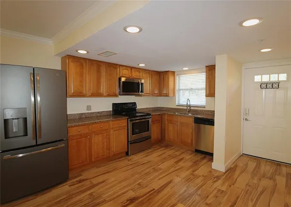 a kitchen with granite countertop wooden floors stainless steel appliances and window