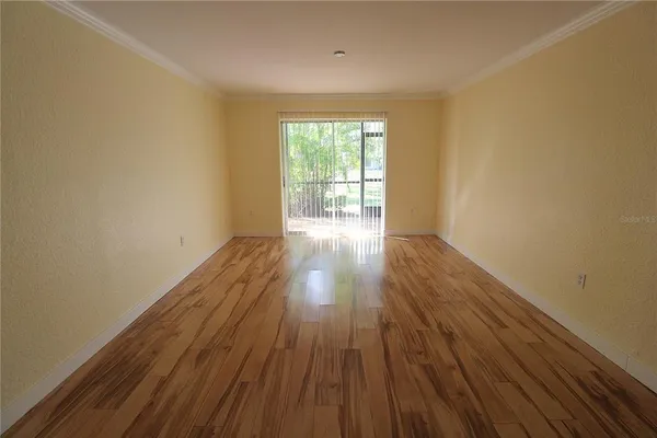 a view of an empty room with wooden floor and a window