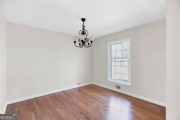 an empty room with wooden floor chandelier and windows