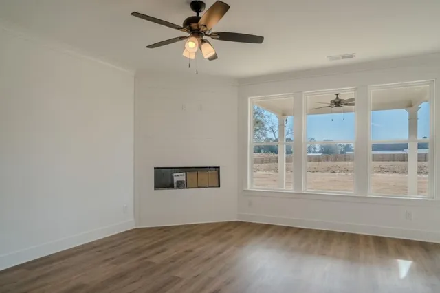 an empty room with wooden floor fan and windows