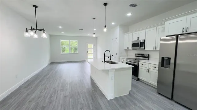 a kitchen with stainless steel appliances a refrigerator a sink dishwasher a stove and white cabinets with wooden floor