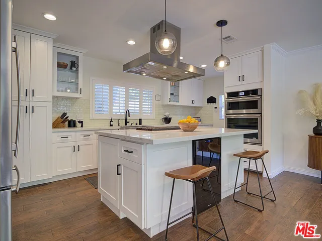 a kitchen with stainless steel appliances a stove a sink a dining table and chairs with wooden floor