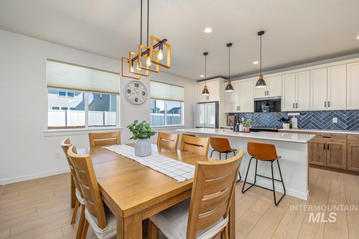 1380 West Chilitna Street Meridian, ID 83642 - Photo 18 of 50 Open-concept dining and kitchen area featuring wood-finish flooring, a modern linear chandelier, recessed lighting, white perimeter cabinetry, and a large kitchen island with pendant lighting and counter seating
