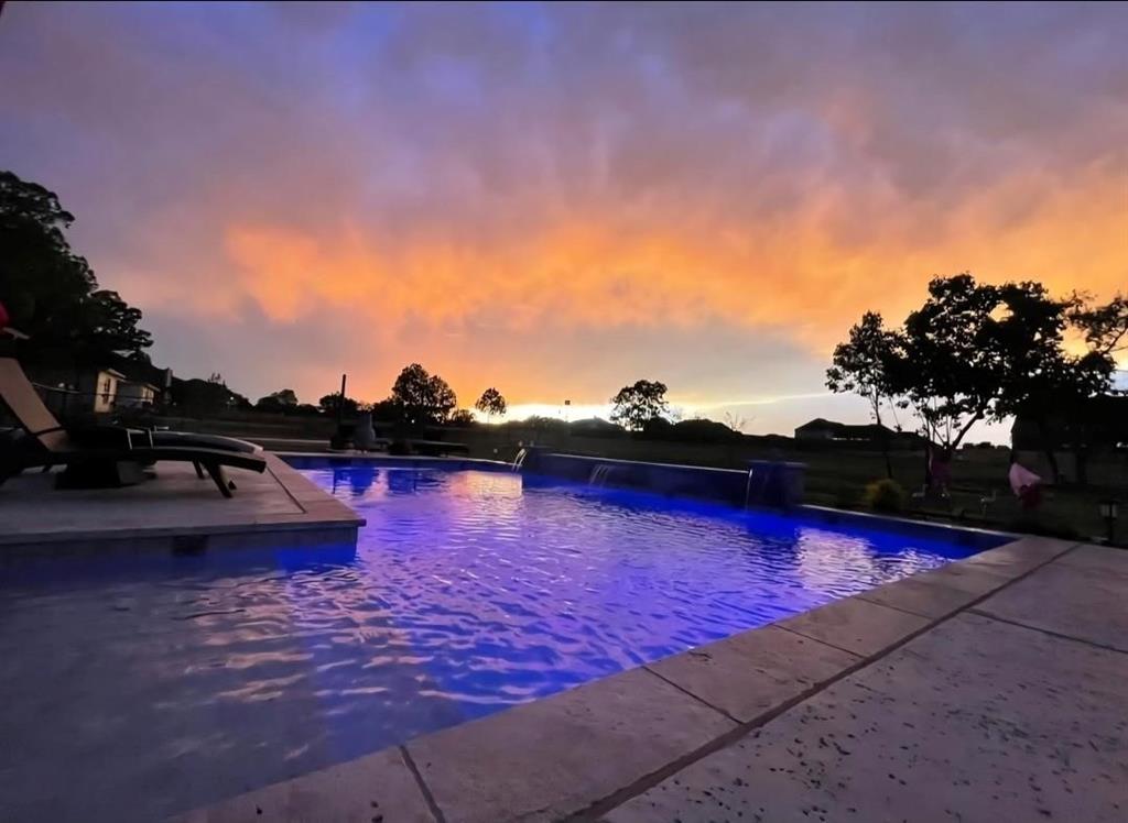 The property features an illuminated swimming pool with an integrated waterfall feature and surrounding stone coping
