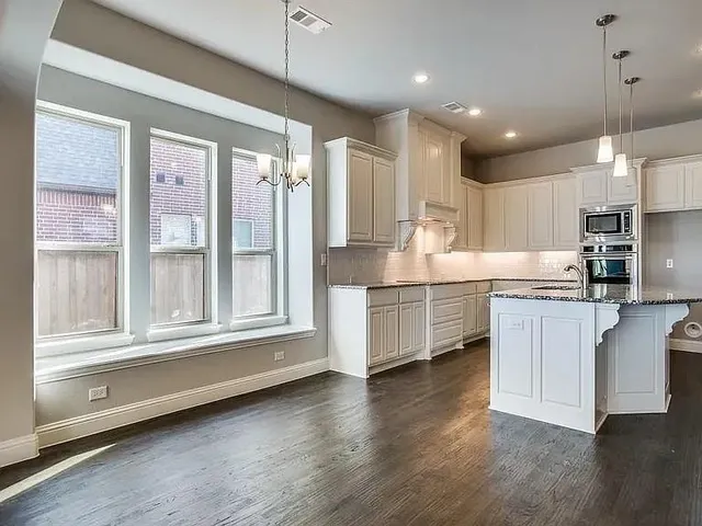a kitchen with stainless steel appliances granite countertop a stove a sink and white cabinets with wooden floor